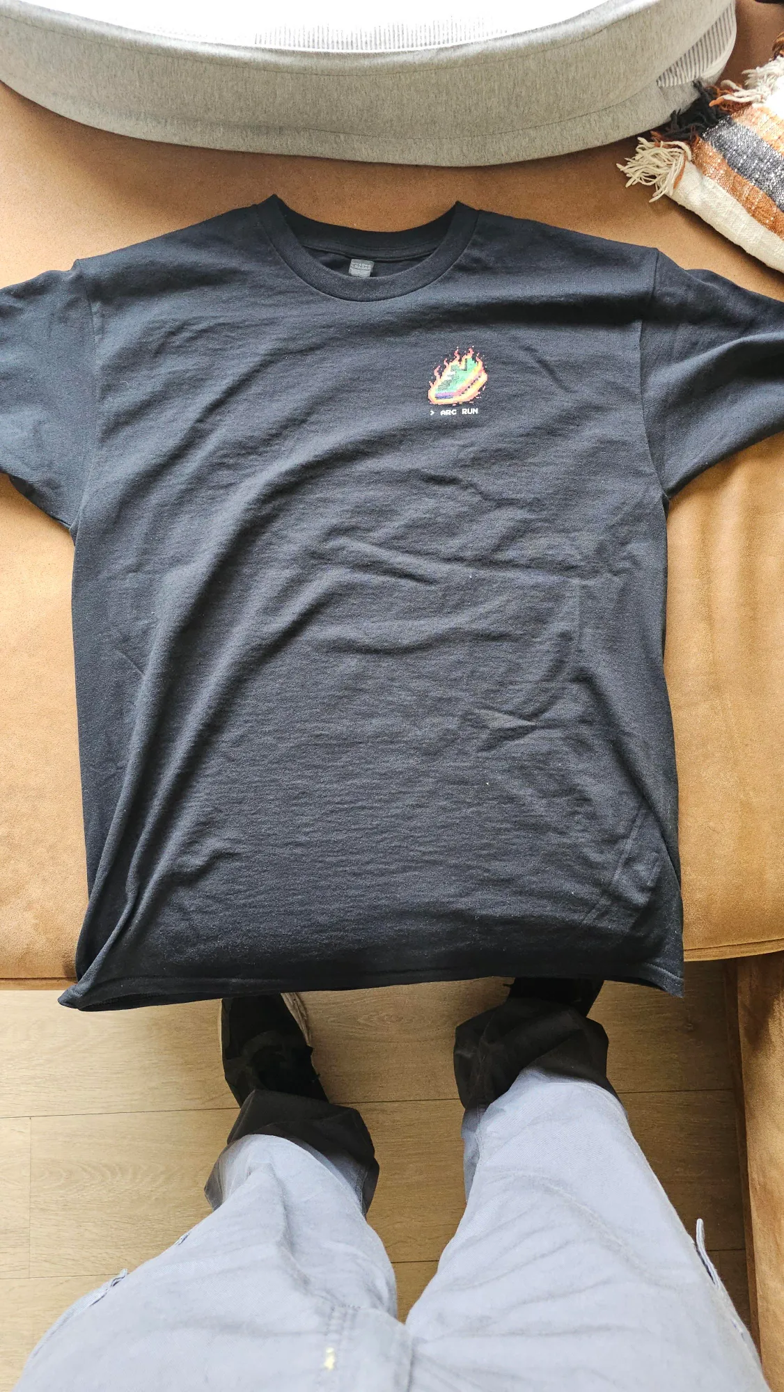 A black Arc Run t-shirt laid flat, with the pixel flaming sneaker on the chest